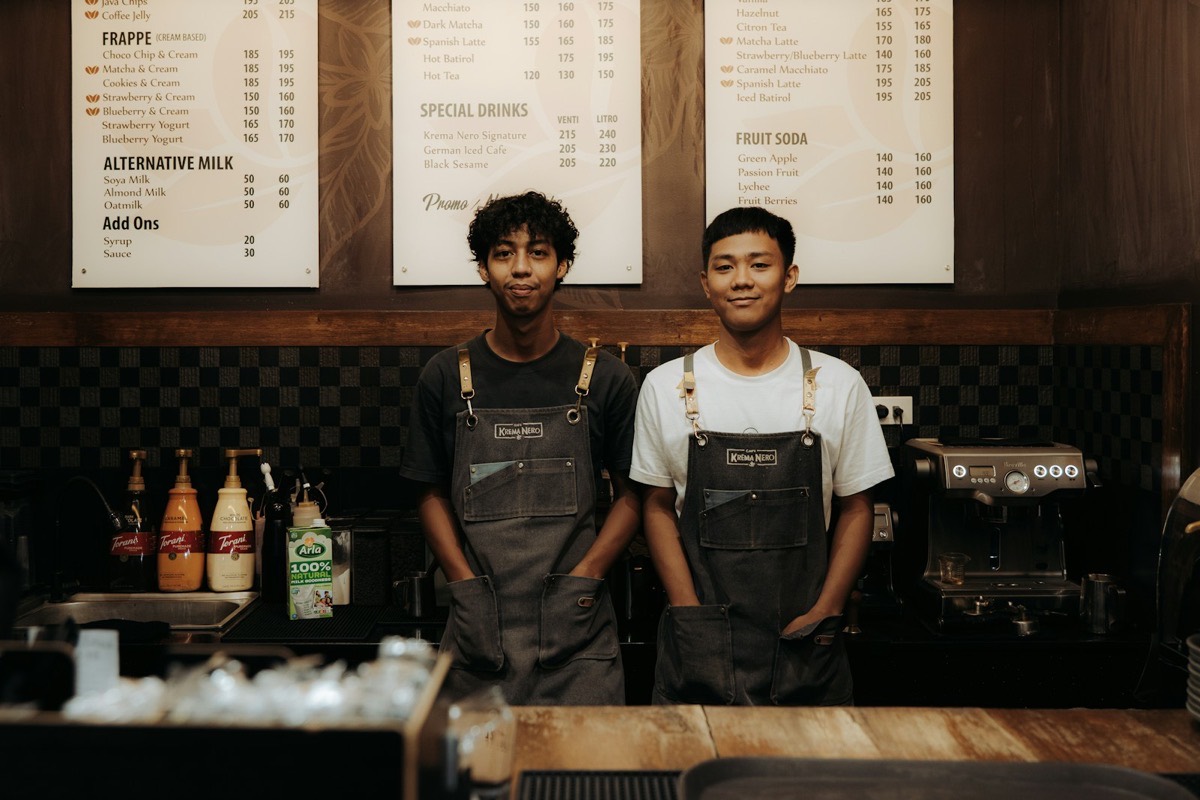 Two smiling baristas standing behind their coffee shop counter