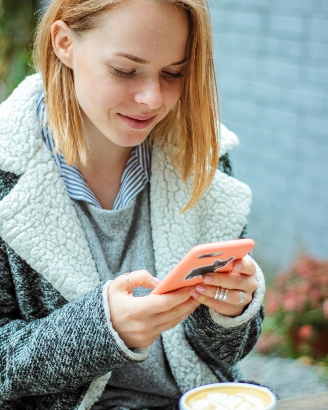 A young woman smiles at her phone next to a cup of coffee