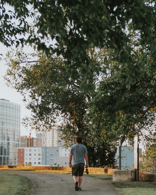 A man walks along a tree-lined park path toward the city
